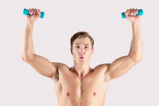 Strength workout. Handsome muscular man lifting small dumbbells on light studio background. Portrait of determined bodybuilder exercising with weights, leading healthy lifestyle photo
