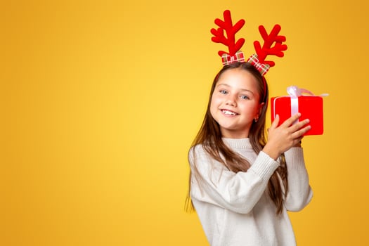 Christmas, holidays and childhood. Happy girl with horns and sweater listens gift, copy space, studio shoot photo