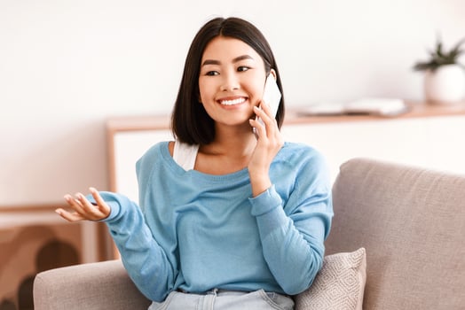 Phone Call. Portrait of smiling asian lady talking on cellphone, resting on couch in living room at home. Communication Concept. Cheerful woman having pleasant conversation, sharing news with friend photo