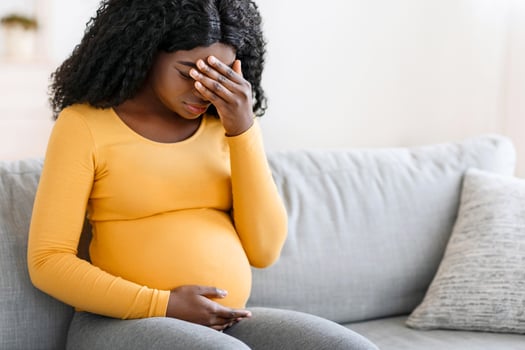 Black pregnant woman suffering from headache at home, sitting on couch, touching her forehead and belly. African american expecting lady having migraine, staying alone at home, copy space photo