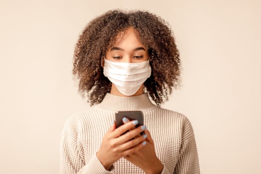 Modern blog about health and coronavirus epidemic. African american woman in white protective mask texting on smartphone about quarantine with followers on social media, isolated on light background photo