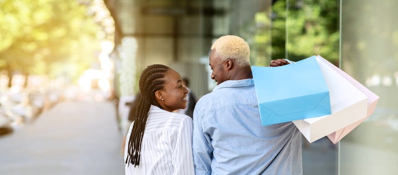 Shopaholics in city. Happy african american couple with many colored bags walking from store after shopping, outdoors, copy space, back photo