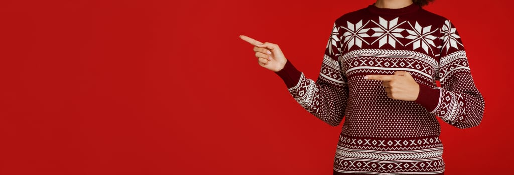 Advice for Christmas and New Year sale at winter holidays. African american lady in sweater with pattern points fingers at empty space, isolated on red background, panorama, cropped, studio shot photo