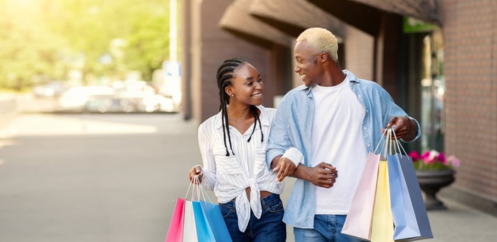 Travel and shopping in city. Cheerful african american young man and woman with colored bags go from mall and discuss purchases photo