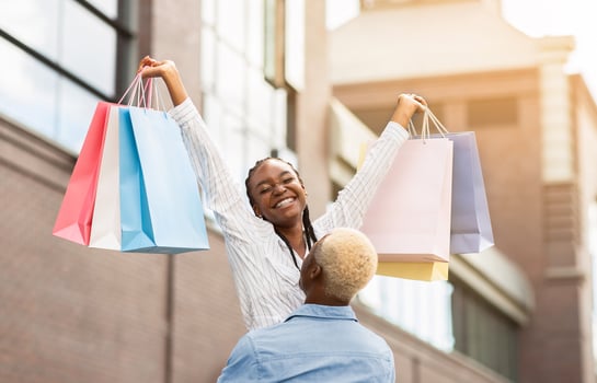 Happy moments on walk together. African american millennial guy picks up woman with colored bags near boutique, sun flare photo