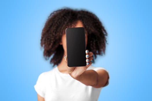 Excellent result, win in online game and great offer. Unrecognizable teen african american female shows blank screen of phone to camera, isolated on violet background, free space, studio shot photo