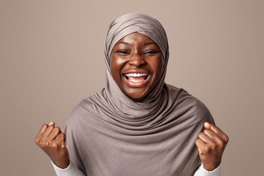 Euphoric black muslim lady in in hijab celebrating success, shaking clenched fists an exclaiming with excitement at camera, emotional african islamic woman posing over light background, empty space photo