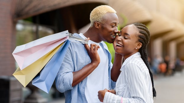 Secrets of fashion bloggers. Cheerful african american man and woman with colored packages near shop, outdoors photo