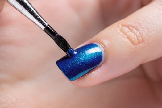 A person is using a brush to apply blue nail polish photo