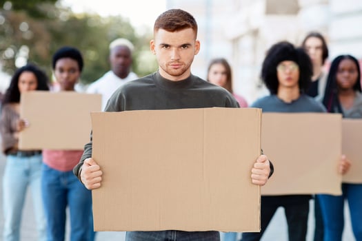 Confident guy leading international group of demonstrators on the street. Young man activist over multiracial group of people with empty placards protesting for human or animal rights photo
