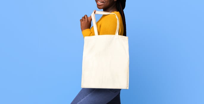 Blank eco tote canvas bag for mockup design in hands of positive black woman standing over purple background in studio and smiling at camera, ecology or environment protection concept, copy space photo