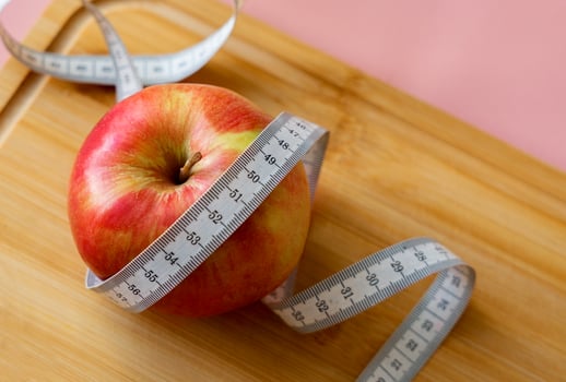 Red apple with measuring tape on wooden board, diet, weight loss concept, healthy eating. Soft focus. photo