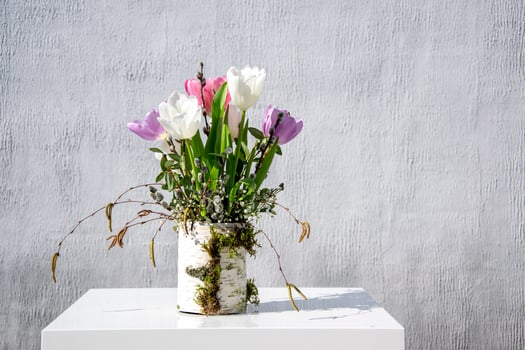 Colorful tulips in shades of purple and white bloom from a textured vase, adding freshness to a minimalist setting photo