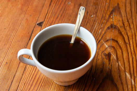 Minimalist top view of a white coffee cup with etal spoon placed on a textured wooden table or windowsill surface. 08 photo
