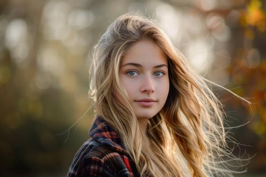 Blonde teenager girl posing in autumnal park with hair blowing in wind photo