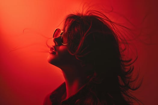 Fashion model wearing sunglasses posing with red light and blowing hair photo
