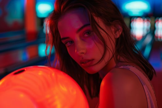 Young woman bowling in neon lit alley holding glowing red ball photo