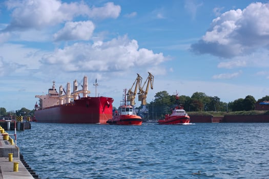 Cargo ships and tugboats maneuvering in a busy harbor under clear blue skies with a few clouds in the background photo
