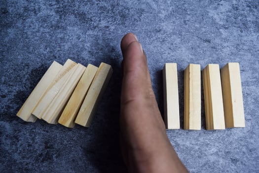 Hand of a businessman stopping domino effect on wooden blocks photo