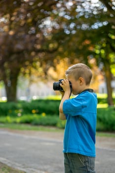 Cute boy in a blue T-shirt takes photos with a camera in a city park