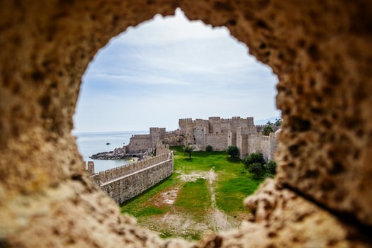 View of a historic fortress through a circular stone opening, showcasing its architectural beauty and green surroundings under a clear sky. photo