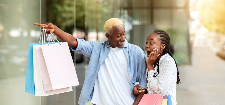 Wow, brand store and sale. Shocked african american girl with open mouth and with packages, and man points to shop window, outdoors photo