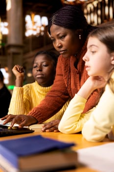 African american professor mentoring diverse students in the library, learning together in an academic library filled with curriculum books. Woman tutoring her class pupils on literature subject. photo