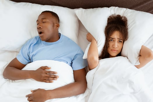 Snoring man sleeping with apnea and sleepless woman, angry wife unable to get to sleep. Upset young african american lady covers ears with pillow so as not to hear noise from snoring guy in bedroom photo