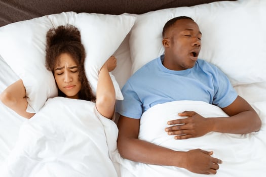Family problems, apnea and insomnia due spouse. Young tired african american guy sleeping and snoring, unhappy sleepless woman covers her ears with pillow so as not to hear noise, empty space photo