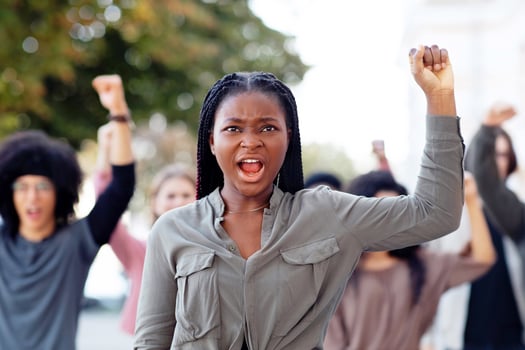 Black woman raising fist up and yelling, leading international group of demonstrators. African american lady leader standing in front of multiracial group of protestors on the street, chanting slogans photo