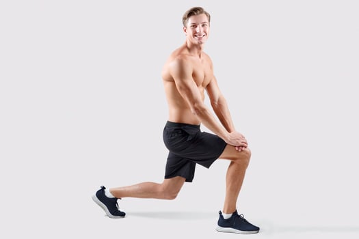 Shirtless millennial guy with bare torso doing lunges on light studio background, full length. Happy young sportsman with sexy body stretching his legs, working out, promoting healthy living photo