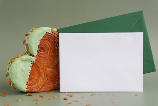 Empty template paper note with envelope greeting card mock up. Heart shaped pistachio croissant on green background with copy space. Puff pastry new trendy sweet dessert bakery. Creamy dough experiment photo