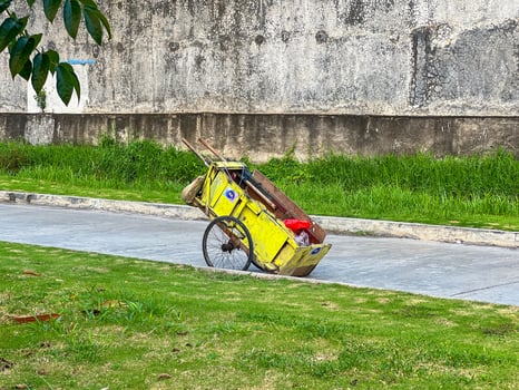 A bright yellow cart is making its way down a road that runs parallel to a lush grassy area filled with vibrant green plants and flowers photo