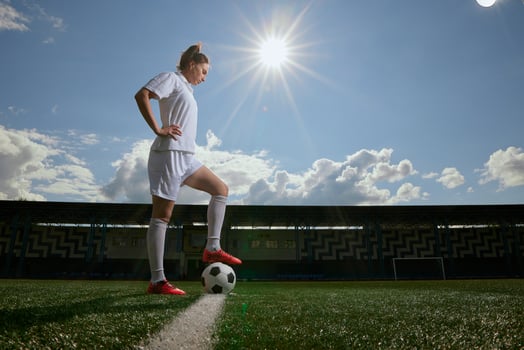 Woman footballer poses with soccer ball under sunny sky on outdoor stadium field. photo