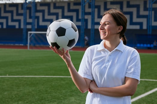 Young woman athlete balancing soccer ball on finger at stadium, smiling confidently. photo