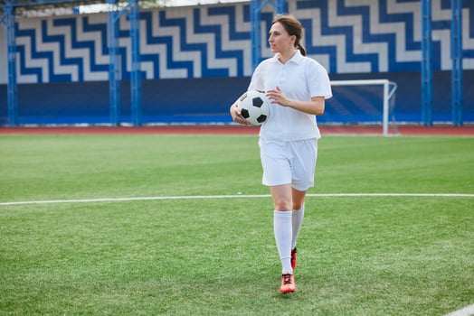 Woman in soccer uniform holding ball, walking confidently on green field. photo