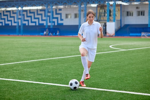 Young woman in white sportswear practices soccer ball control on green field. photo