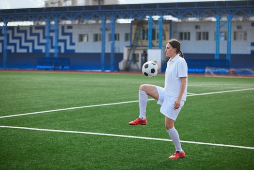 Focused woman juggling soccer ball on green football field during training session. photo