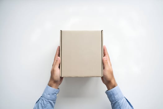 Hands in blue shirt holding beige cardboard box on white photo