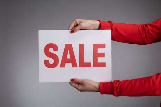 Hands in red sleeves holding white SALE sign on gray photo