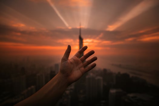 Silhouetted hand reaching toward city skyline at sunset photo