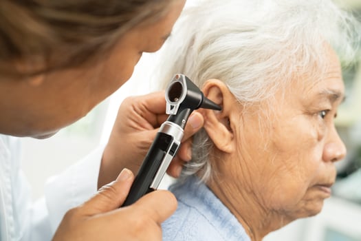 Audiologist or ENT doctor use otoscope checking ear of asian senior patient photo