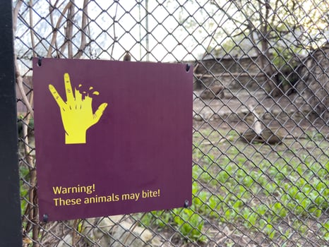 Warning sign on zoo enclosure fence showing bitten hand and message. These animals may bite to caution visitors and promote safety awareness around wild animals photo