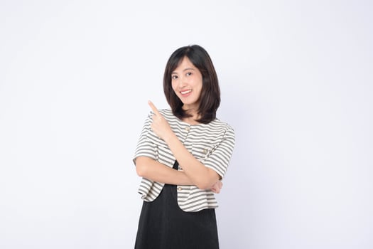 Southeast Asian woman smiling and pointing to side in advertising concept with casual striped jacket and black dress on white background photo