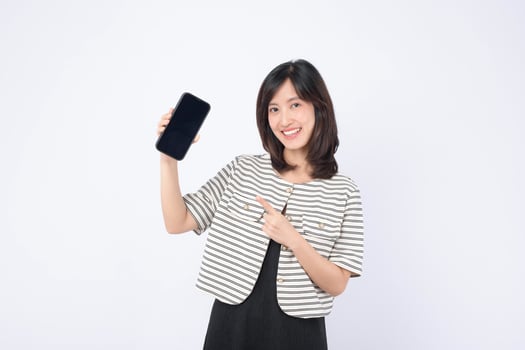 Southeast asian woman happily points at mobile phone screen showing internet application, demonstrating excitement and engagement with digital technology in bright setting photo