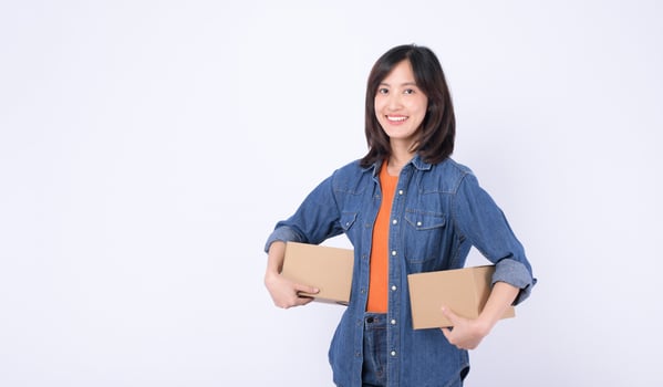 Southeast asian woman is happily shopping online holding two cardboard boxes wearing casual denim clothes and orange shirt against white background photo