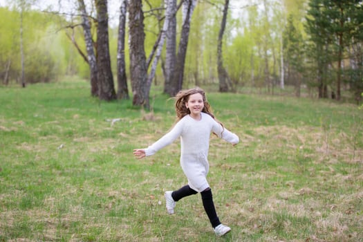 A little girl runs through the spring forest. A child on a walk in the park. photo