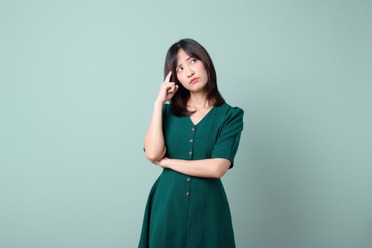 Southeast asian woman in green dress poses thoughtfully for advertising with calm expression against plain light blue background photo