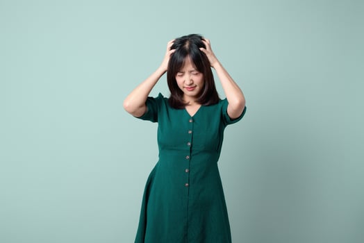 Southeast asian woman in green dress shows frustration holding her head with closed eyes in advertising style photo with plain background