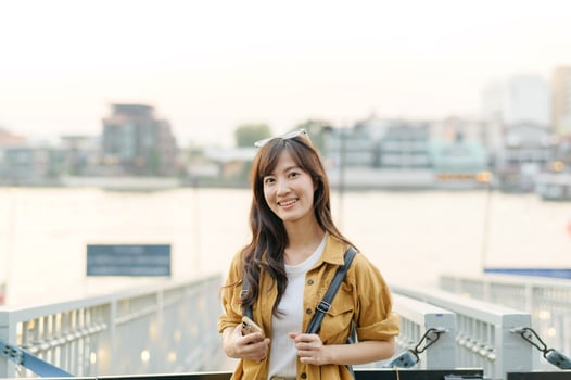 Southeast asian woman smiles happily while travel near river in urban area, capturing joyful travel concept with casual clothing and natural light in background photo